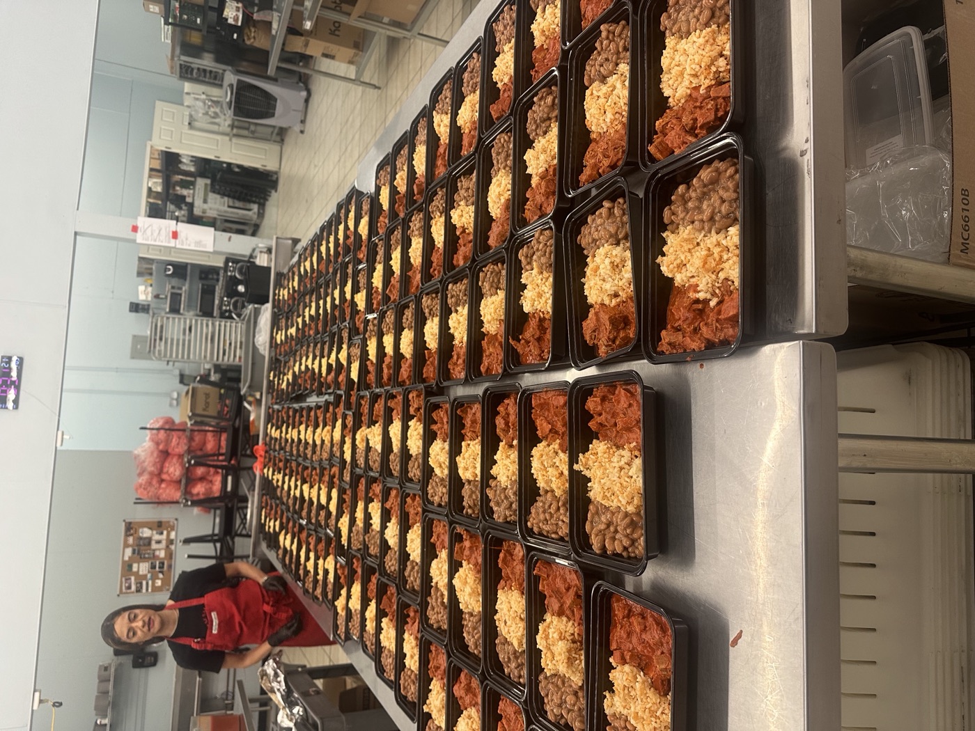 Paz Salsa kitchen staff packing rows of fresh meal prep containers with rice, beans, and meat