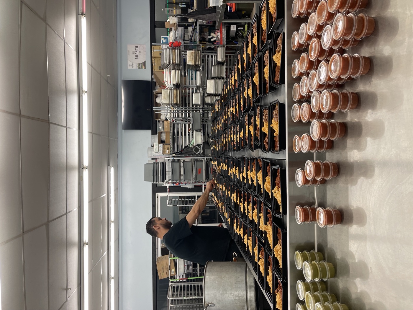 Paz Salsa kitchen staff plating meal prep trays next to stacked cups of fresh salsa